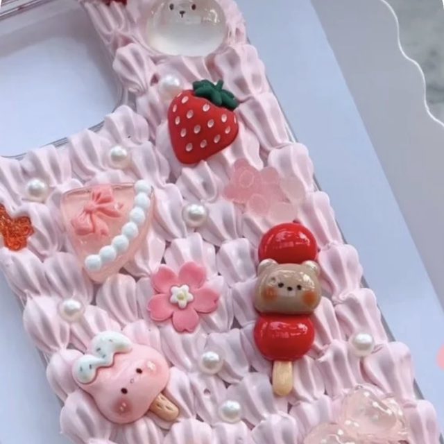 A finished decoden phone case piped in pink whipped cream and covered in a strawberry, a sakura flower, pearls and kawaii charms, made at a Popi party in Melbourne